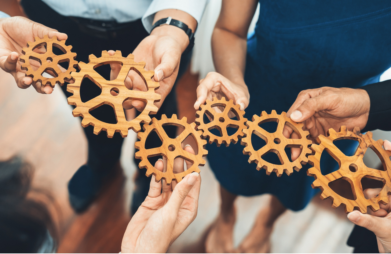 A group of people holding gears that fit together, symbolizing teamwork