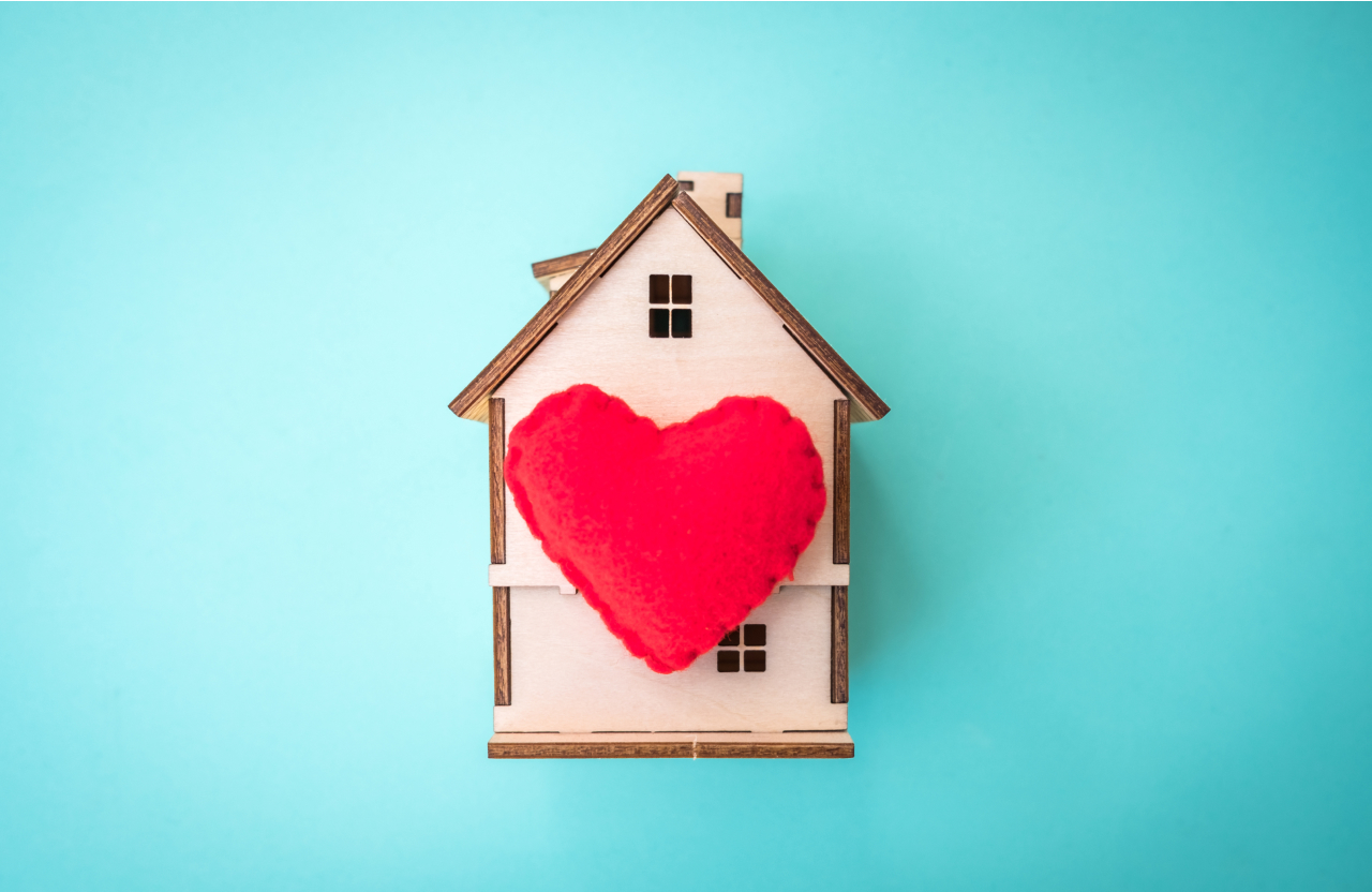 a granite teal background with a tan, wooden model of a house with a read heart in the middle.