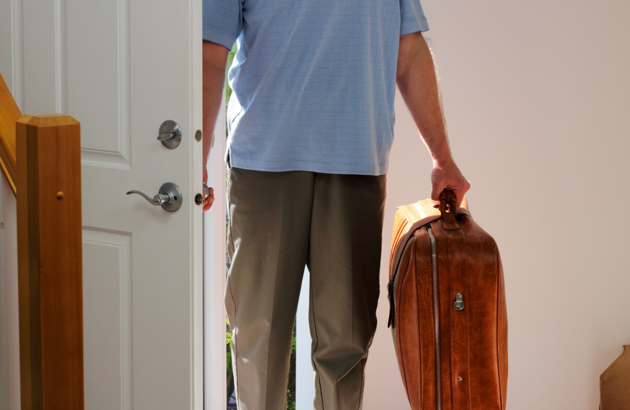 A man walks into a home carrying a suitcase