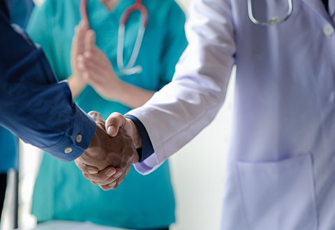 Nurse in background and doctor shaking hands with a patient