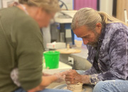 Man helps student shape clay on a potter’s wheel.