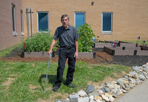 Man with cane standing in front of raised garden beds and beside rock border