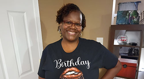 Smiling woman wearing glasses and  black t-shirt standing in front of a door and shelves