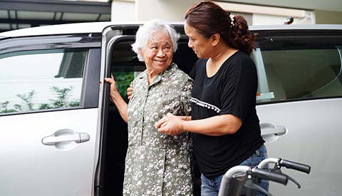 Caregiver helps Asian elderly woman disability patient get in her car, medical concept